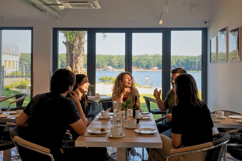 Frühstücksraum des Hotels mit Fensterfront zum Wasser, Menschen an einem langen Tisch
